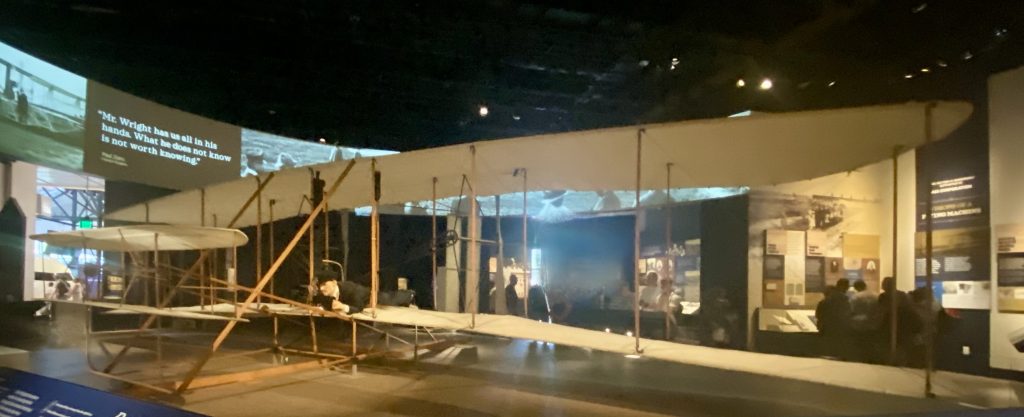 Male mannequin demonstrating how the Wright Flyer biplane was originally flown