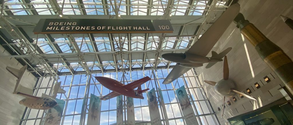 Three small aircraft hanging from the ceiling under a Boeing Milestones of Flight Hall sign