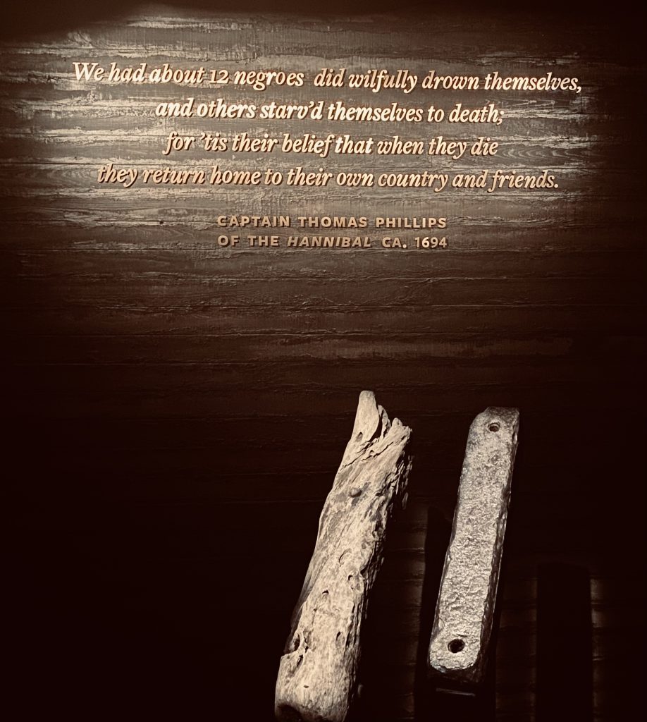 Piece of wood from ship alongside metal brace; quote above pieces says "We had about 12 negroes did willingly drown themselves, and others starved themselves to death; for 'tis their belief that when they die they return home to their own country and friends" Captain Thomas Phillips of the Hannibal 1694