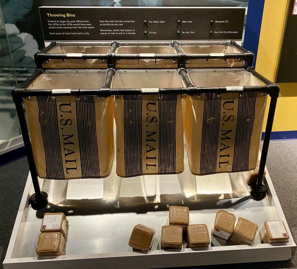 Six bins labeled US Mail with small cardboard boxes