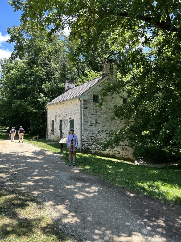 Author standing along dirt path in front of white stone house along C&O Canal in Maryland